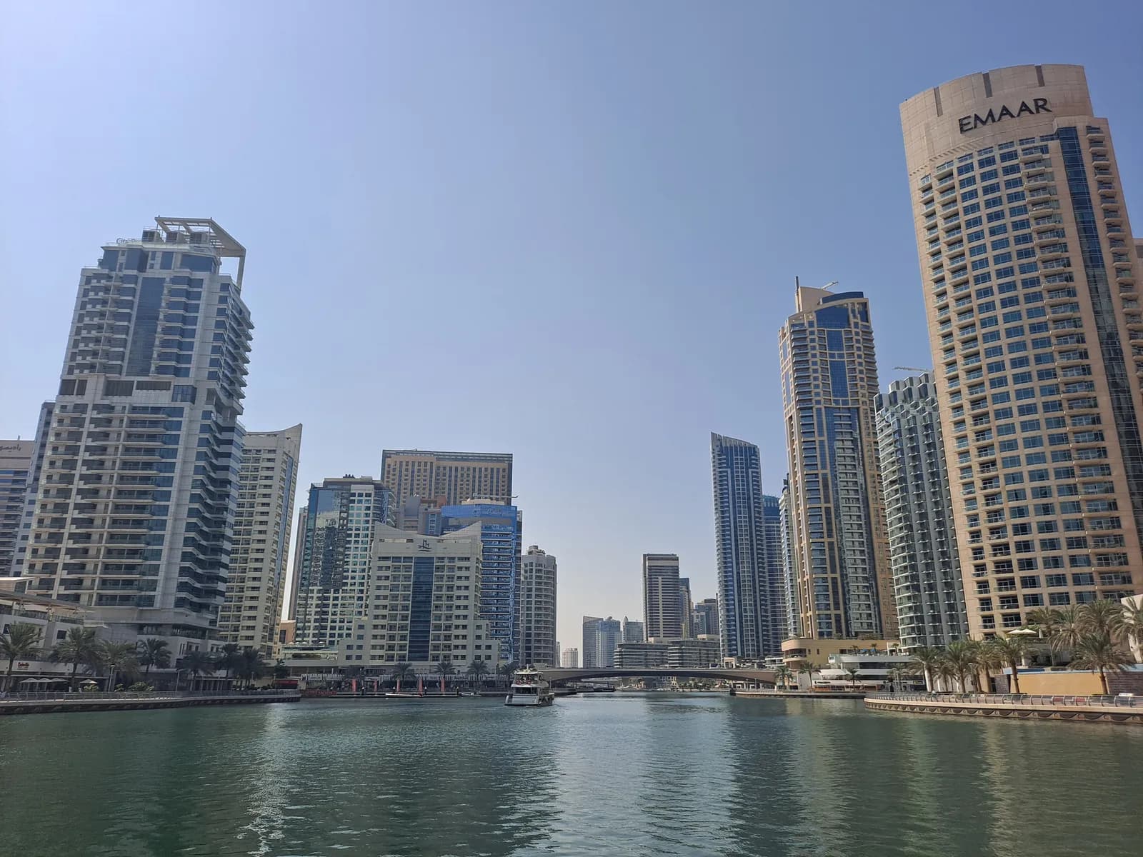 Apartment towers lining the Dubai Marina canal, with a boat and bridge in view